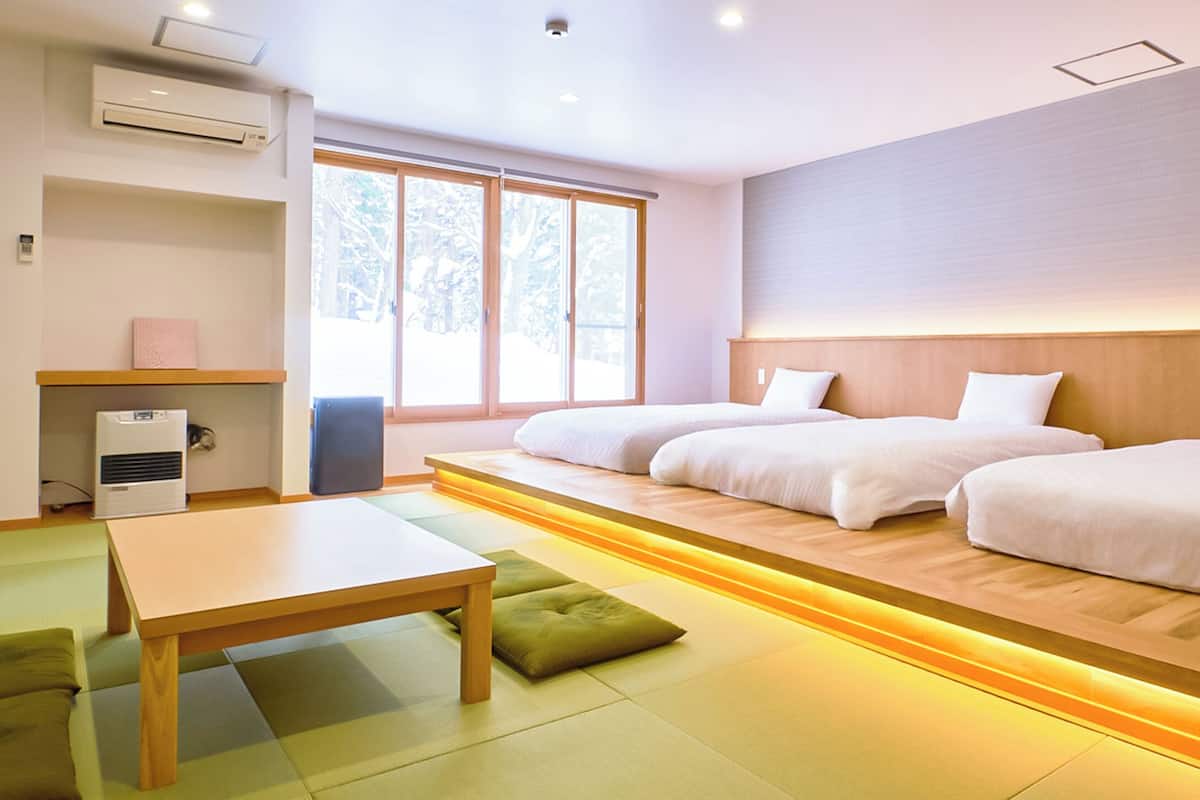 Une chambre d’hôtel avec deux lits, une tête de lit en bois, une petite table et un futon.
