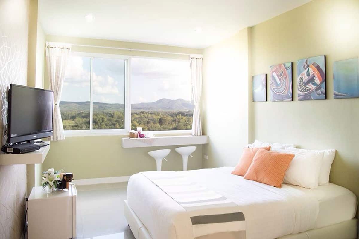 Une chambre à coucher avec un lit, une télévision, une fenêtre donnant sur les montagnes et trois tableaux accrochés au mur.