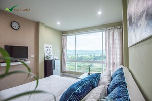 A bedroom with a bed, a TV, a window with curtains, and a view of the outdoors. - Na Loei Boutique Resort Hotel (Mueang Loei)