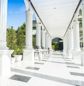 A covered outdoor area with white columns and a tiled floor, featuring outdoor seating and potted plants. - Na Loei Boutique Resort Hotel (Mueang Loei)