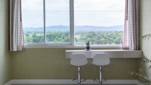 A room with a large window, two white chairs, a small table, and a potted plant. - Na Loei Boutique Resort Hotel (Mueang Loei)