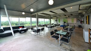 A spacious indoor area with large windows, multiple tables and chairs, and a seating area with a sofa and coffee table. - Na Loei Boutique Resort Hotel (Mueang Loei)