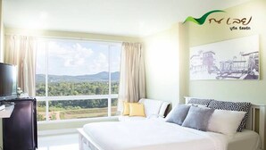 A bedroom with a large bed, a television, and a window with a view of greenery. - Na Loei Boutique Resort Hotel (Mueang Loei)