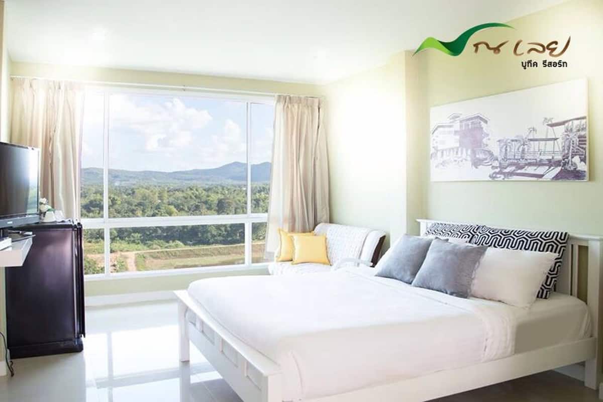 Une chambre avec un grand lit, une télévision et une fenêtre donnant sur un paysage verdoyant.
