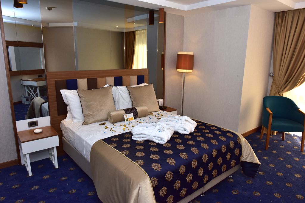 Habitación de hotel con una cama grande, una mesita de noche, una lámpara, una silla y un espejo.