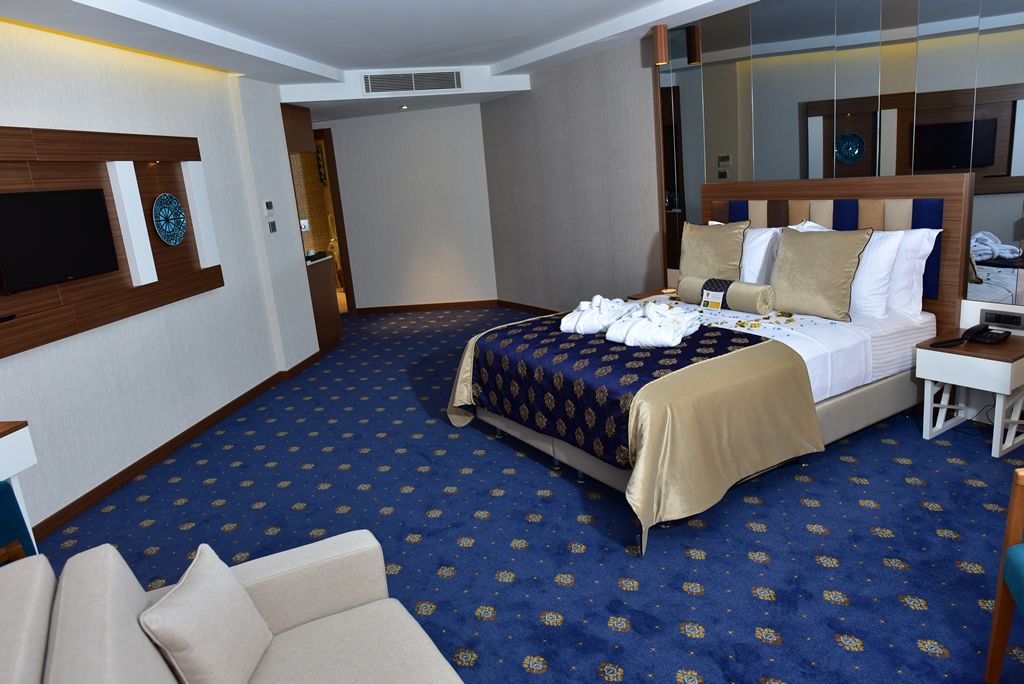 A hotel room with a large bed, a flat-screen TV, a sofa, and a carpeted floor.
