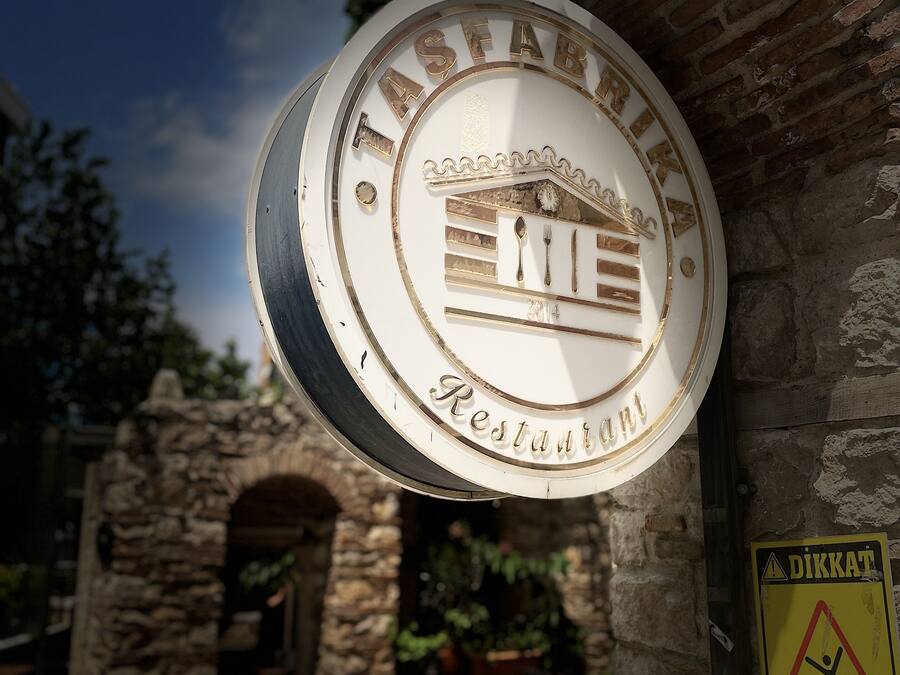 Een restaurantbord met een klassiek ontwerp, een stenen bogenpoort en terrasplekken.