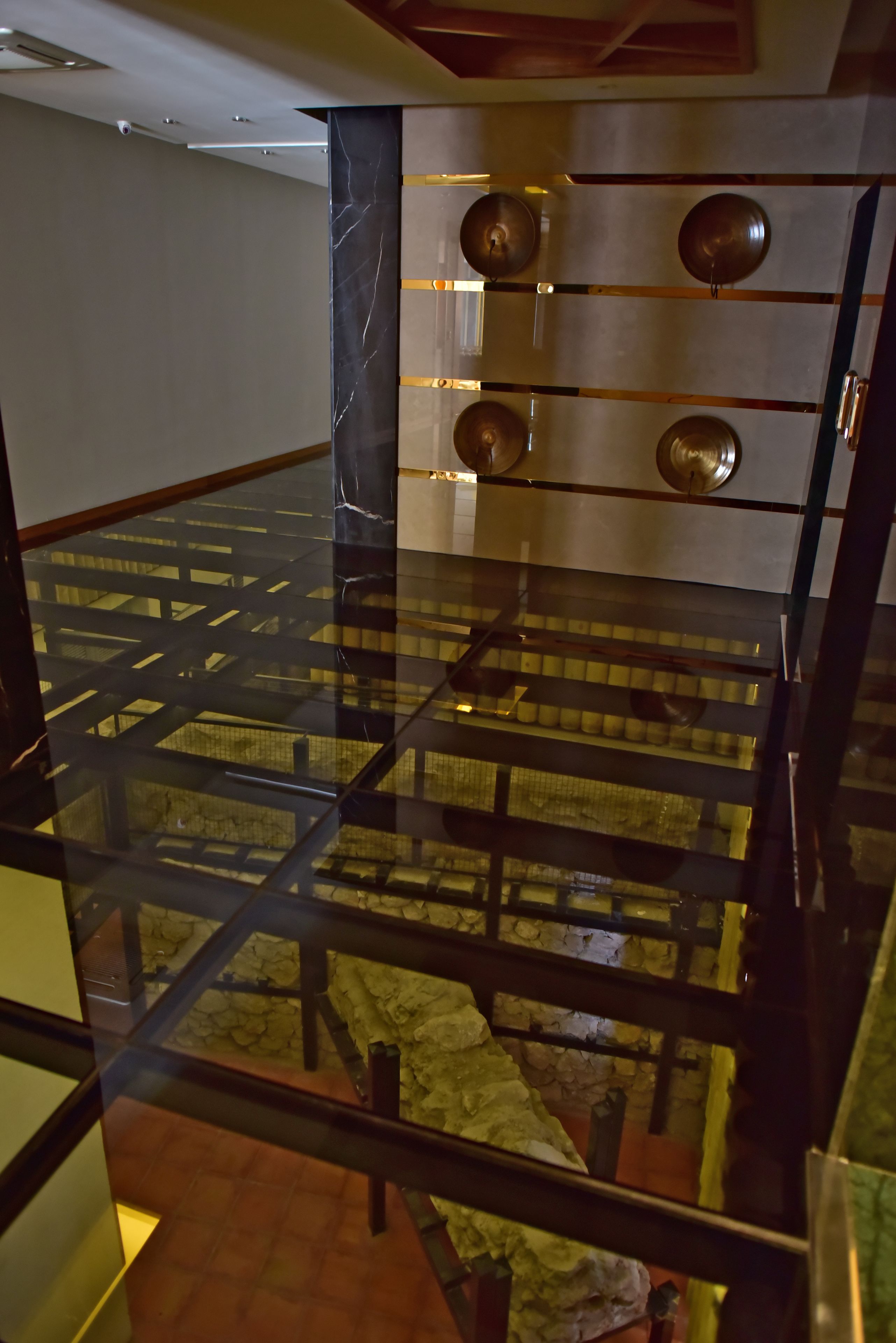 Un interior moderno con piso de vidrio, barandales de metal y pared de piedra.