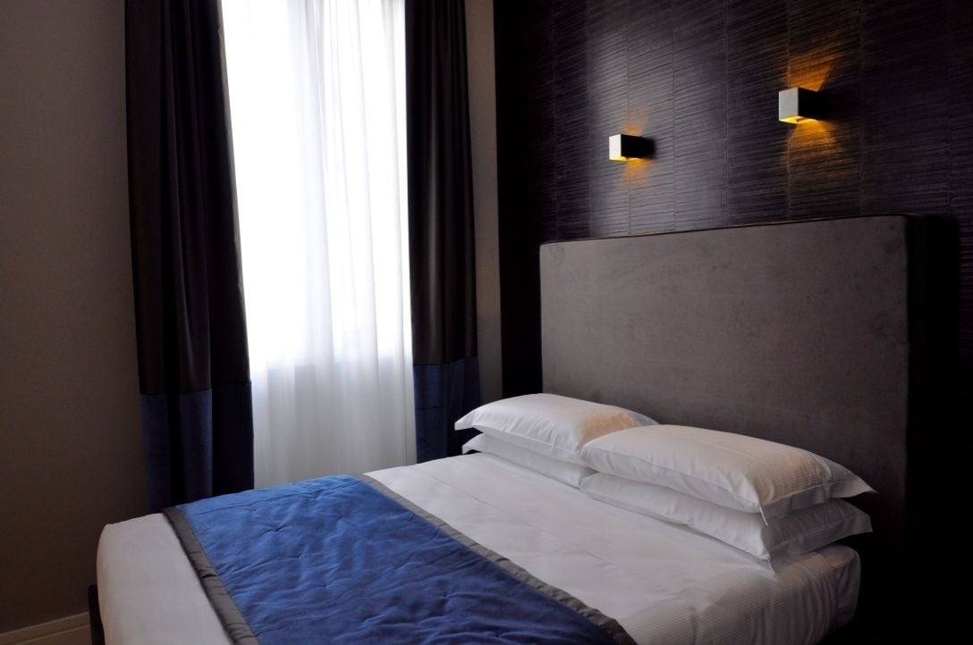 A hotel room with a large bed, dark wall paneling, and a window with curtains.