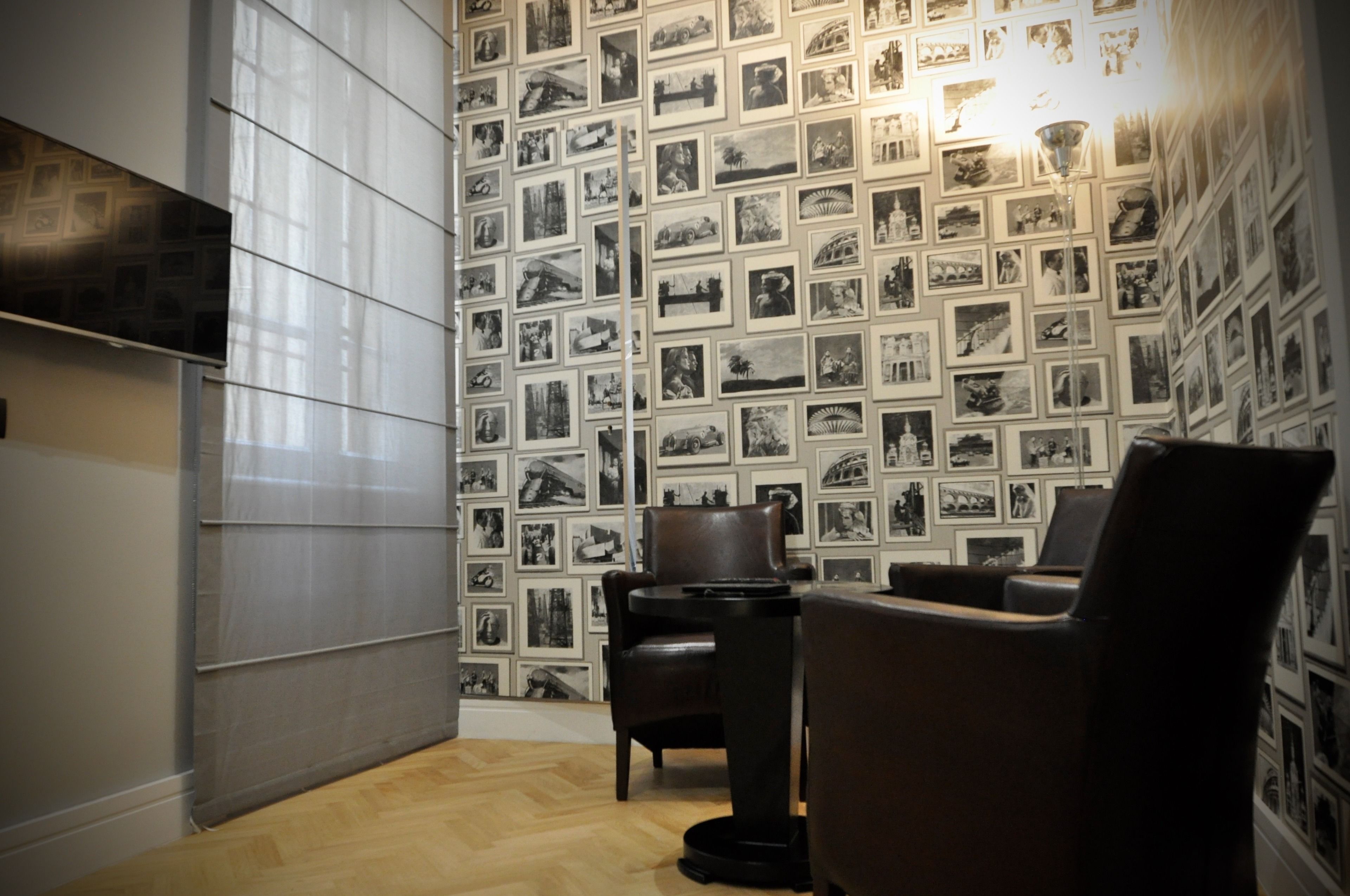 A room with a patterned wallpaper, a wooden floor, and a seating area with chairs.