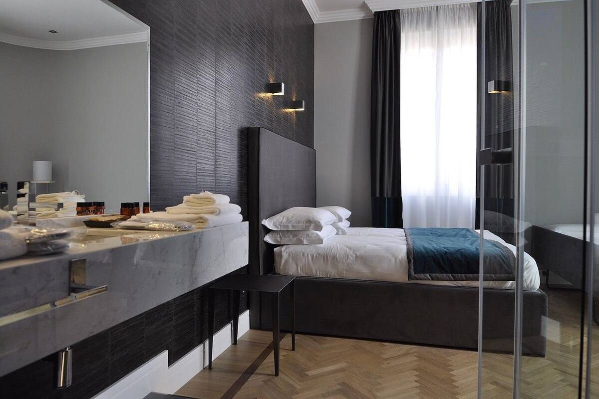 Une chambre d’hôtel moderne, dotée d’un grand lit, d’une table de chevet, d’une coiffeuse avec un miroir et d’une grande fenêtre avec des rideaux.