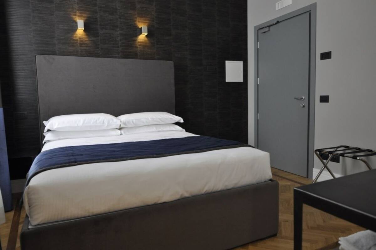 Une chambre d’hôtel moderne avec un grand lit, un mur de couleur sombre et une porte.