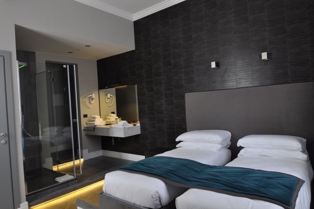 Une chambre d’hôtel moderne avec un grand lit, une douche à l’italienne et un mur texturé de couleur sombre.