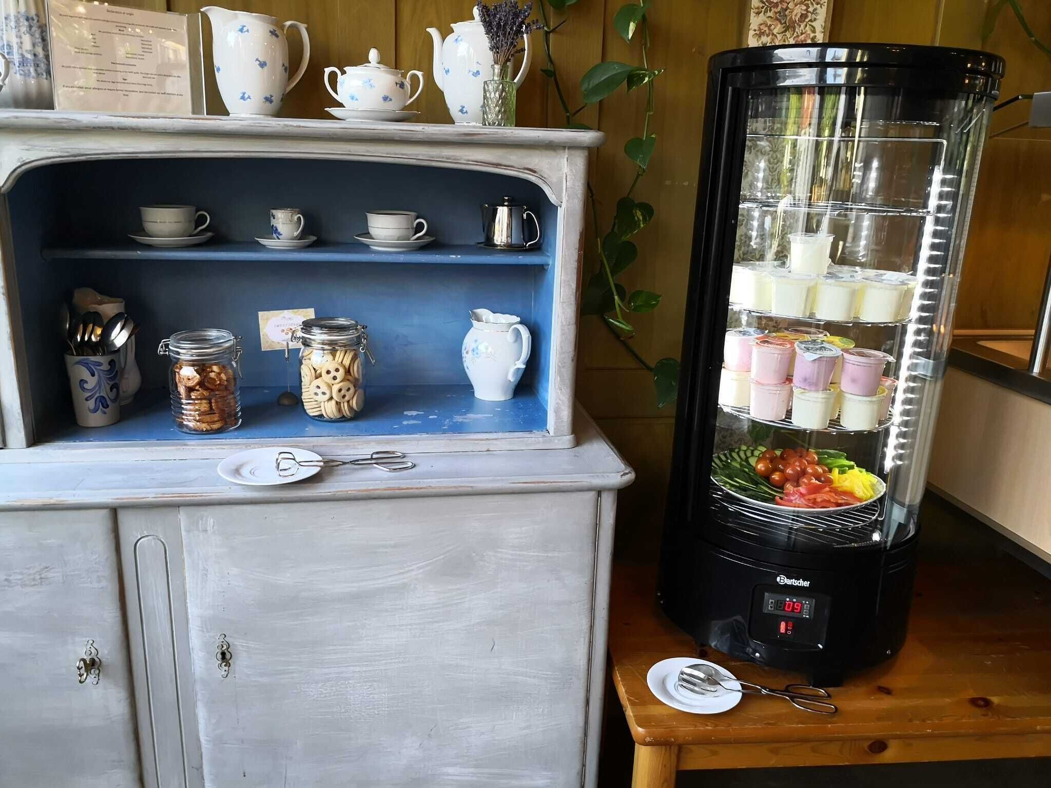 A kitchen area with a coffee maker, a blender, and a shelf with jars and cups.