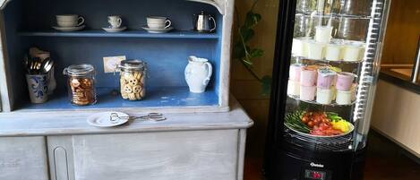 A kitchen area with a coffee maker, a blender, and a shelf with jars and cups.