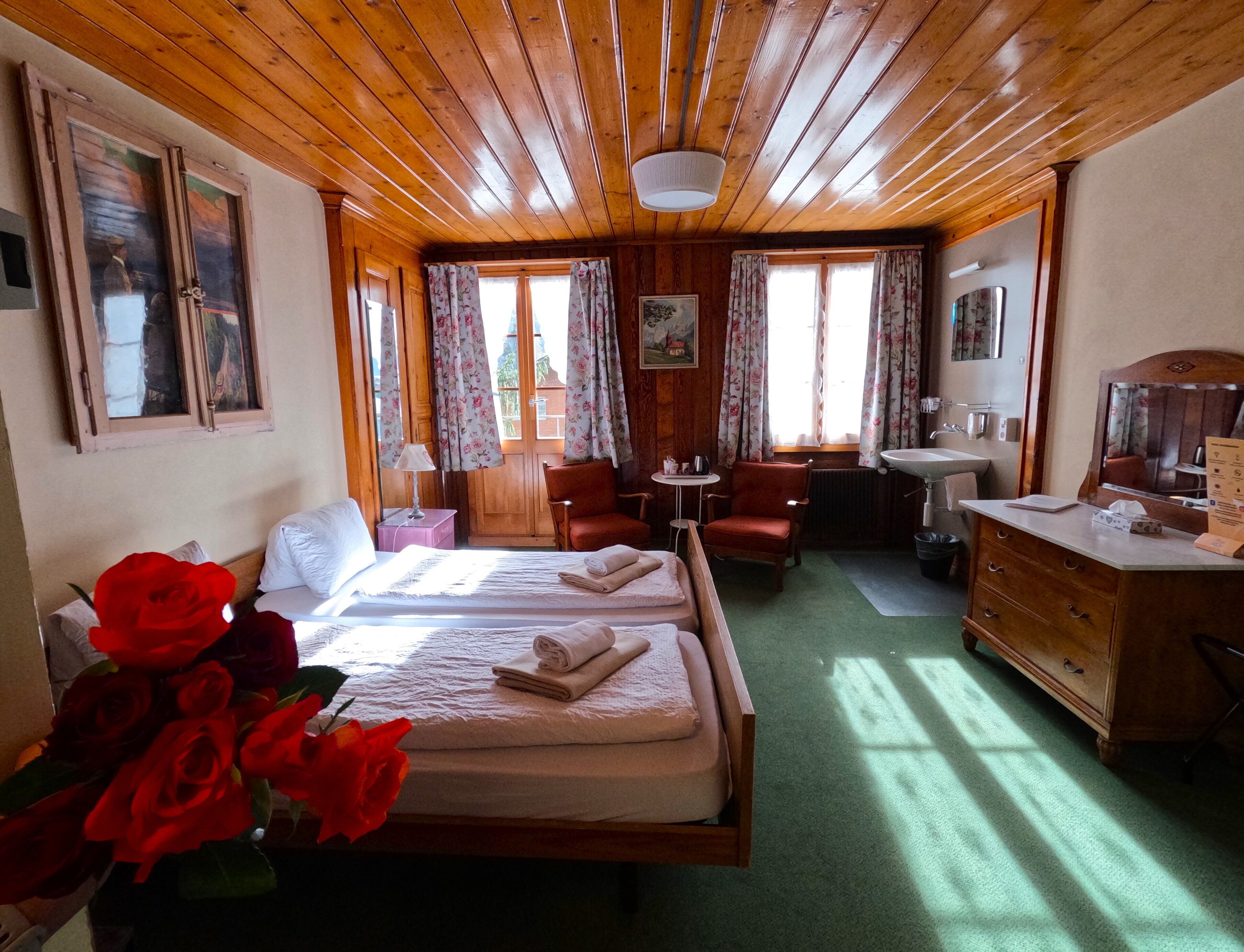 Ein gemütliches Zimmer mit Holzboden, einem Bett mit weißen Leinen, zwei Stühlen, einem kleinen Tisch, einem Waschbecken und einem Spiegel.
