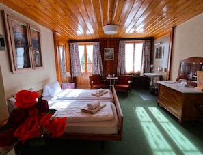 A cozy room with a wooden ceiling, a bed with white linens, two chairs, a small table, a sink, and a mirror.