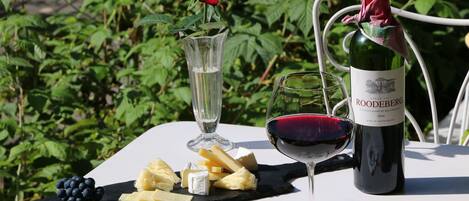 Una mesa con una botella de vino, una copa de vino tinto, una rosa en un jarrón y una selección de quesos y uvas.