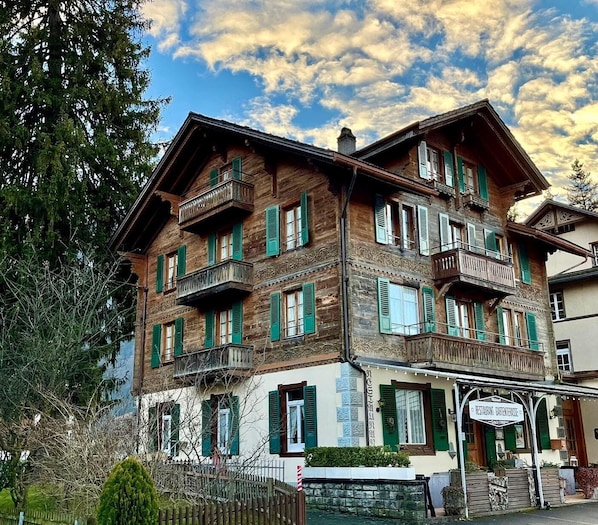A traditional wooden building with multiple balconies and green shutters, likely a hotel or guesthouse.