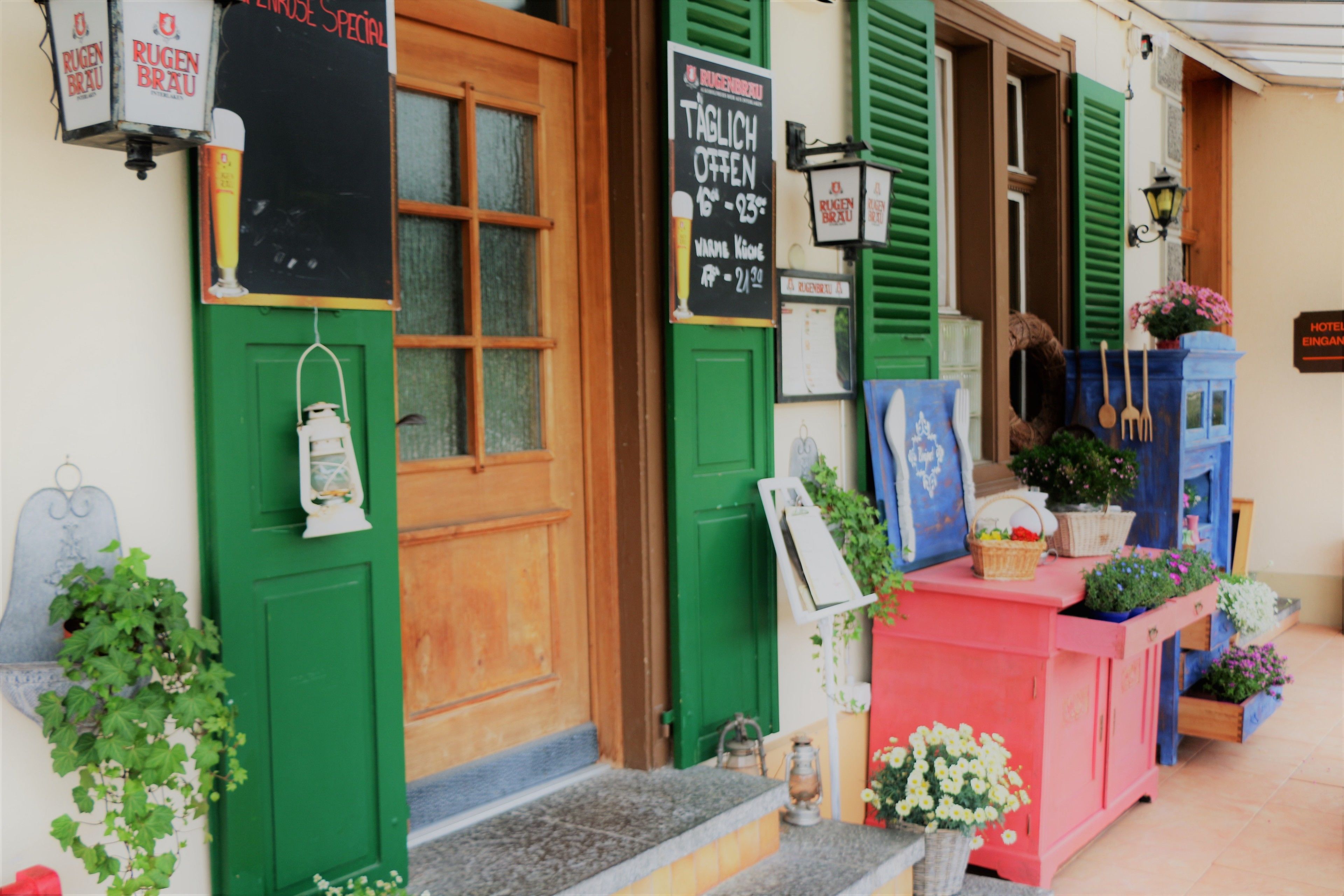 L’entrée d’un hôtel avec des volets verts, une porte en bois et un comptoir rose agrémenté de plantes.