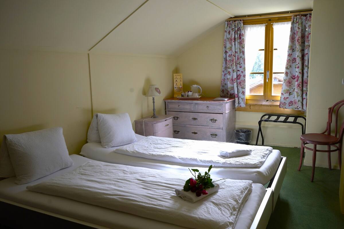 Habitación con dos camas, un aparador, una silla y una ventana con cortinas florales.