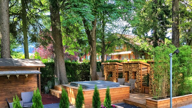 Un belvédère en bois doté d’un jacuzzi, entouré de jardini ères en bois remplies de plantes vertes et de fleurs.