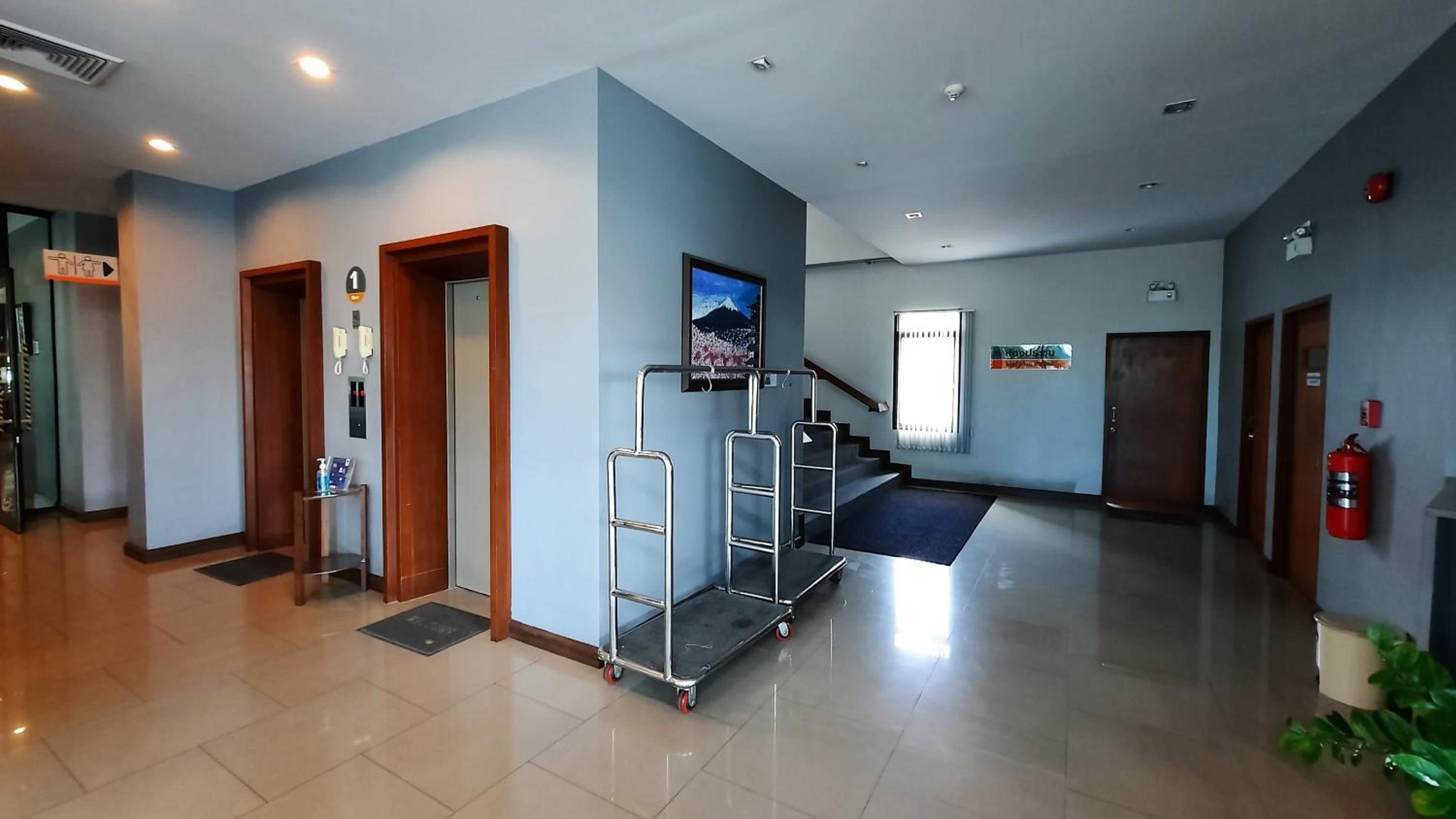 Un vestíbulo moderno y limpio con un mostrador de recepción, un teléfono, una pantalla digital, una escalera y un extintor.