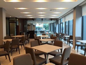 A modern dining area with tables and chairs, large windows, and a view of the outdoors. - Leosor Hotel (Nakhon Ratchasima)
