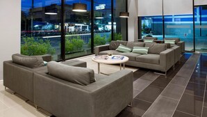 A modern lounge area with two grey sofas, a round coffee table, and large windows offering a view of the cityscape. - Leosor Hotel (Nakhon Ratchasima)