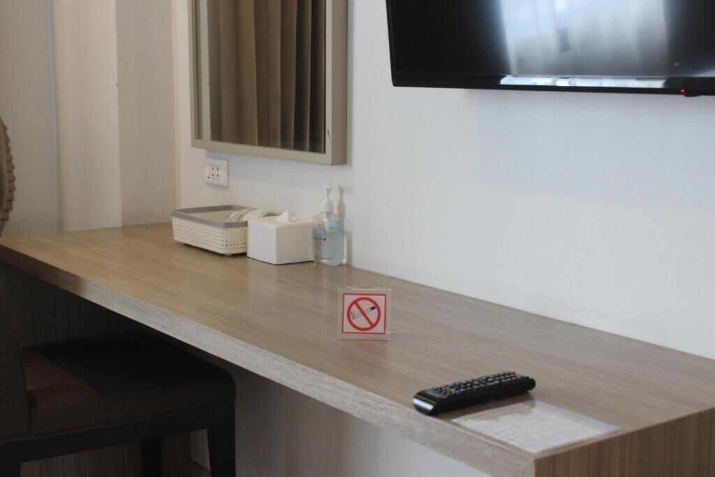 A hotel room with a wooden desk, a television mounted on the wall, a remote control on the desk, and a no-smoking sign.