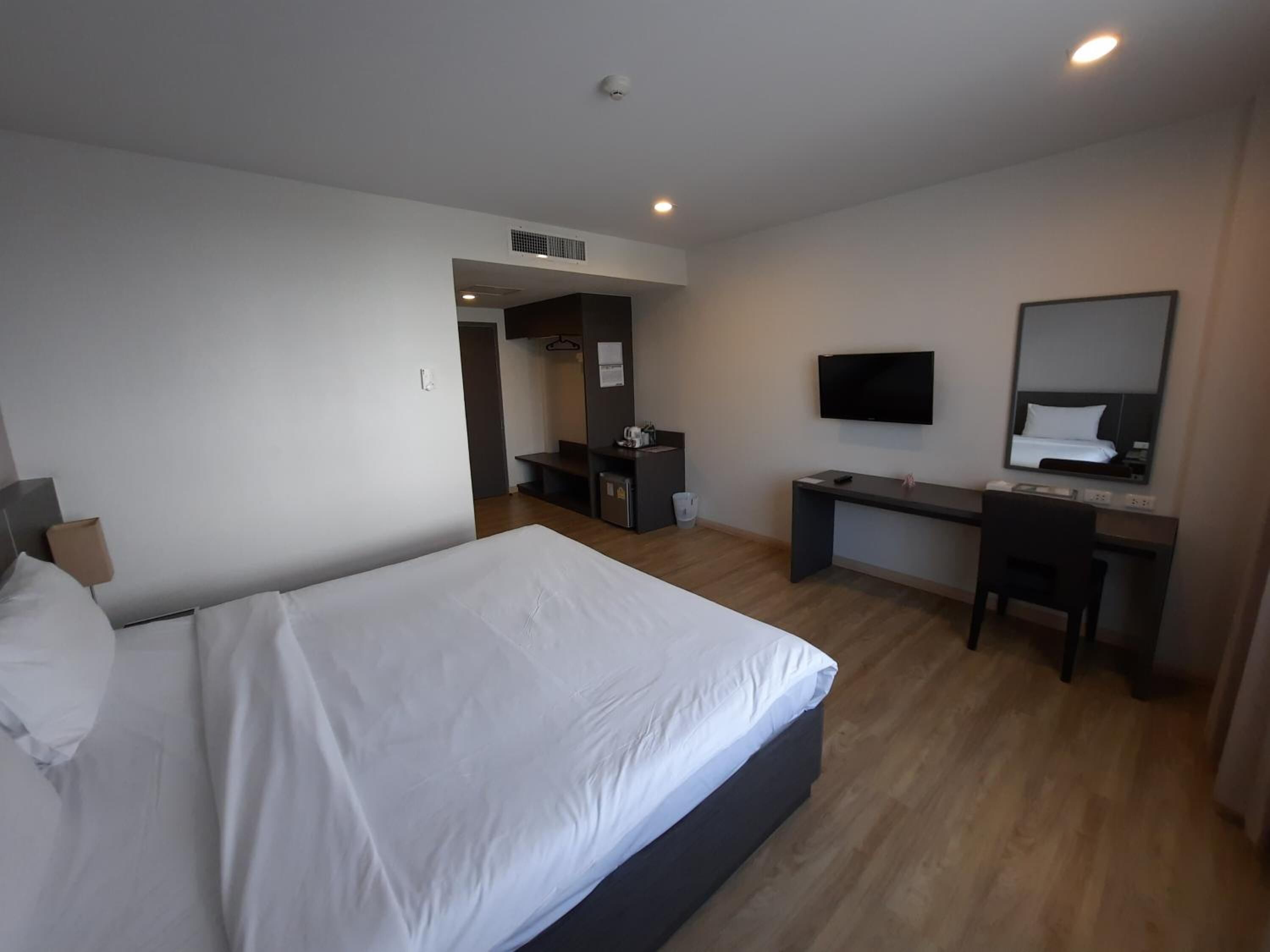 A hotel room with a bed, a desk, a chair, a TV, and a mirror.