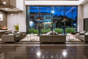 A modern lobby with a large glass wall, a sofa set, and a coffee table. - Leosor Hotel (Nakhon Ratchasima)