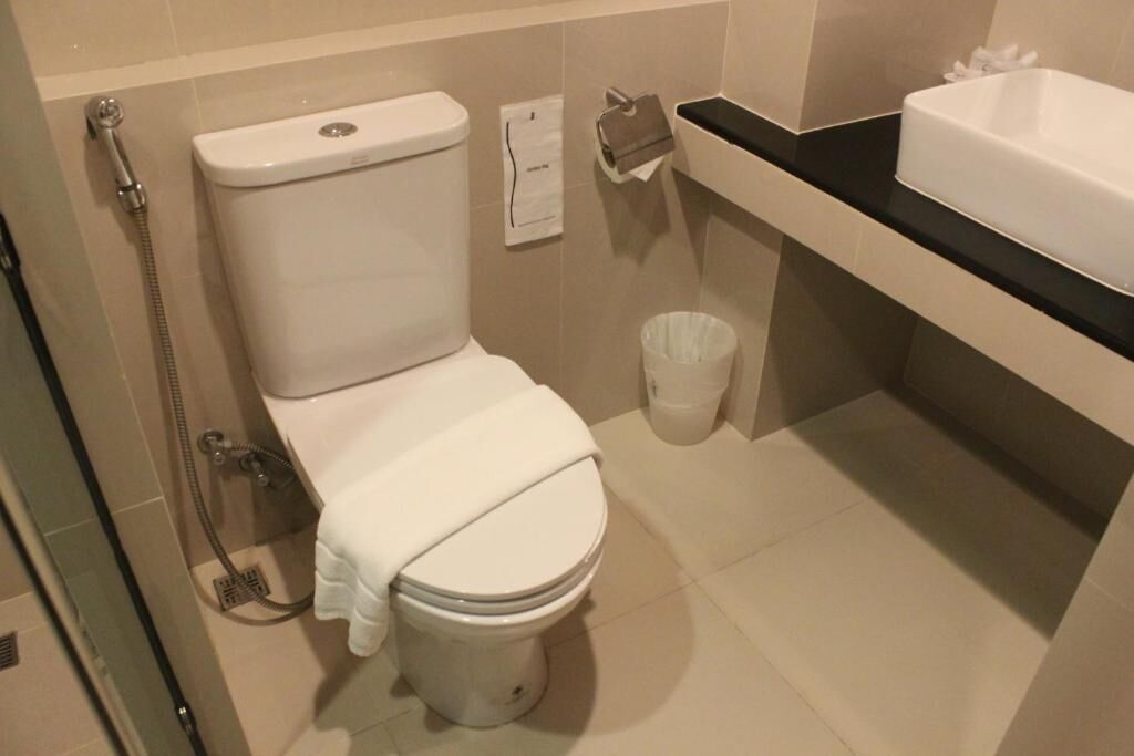 A bathroom with a toilet, a shower, a sink, and a trash bin.