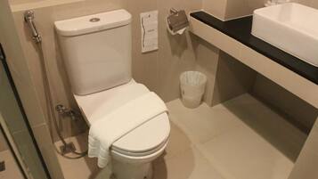A bathroom with a toilet, a shower, a sink, and a trash bin.