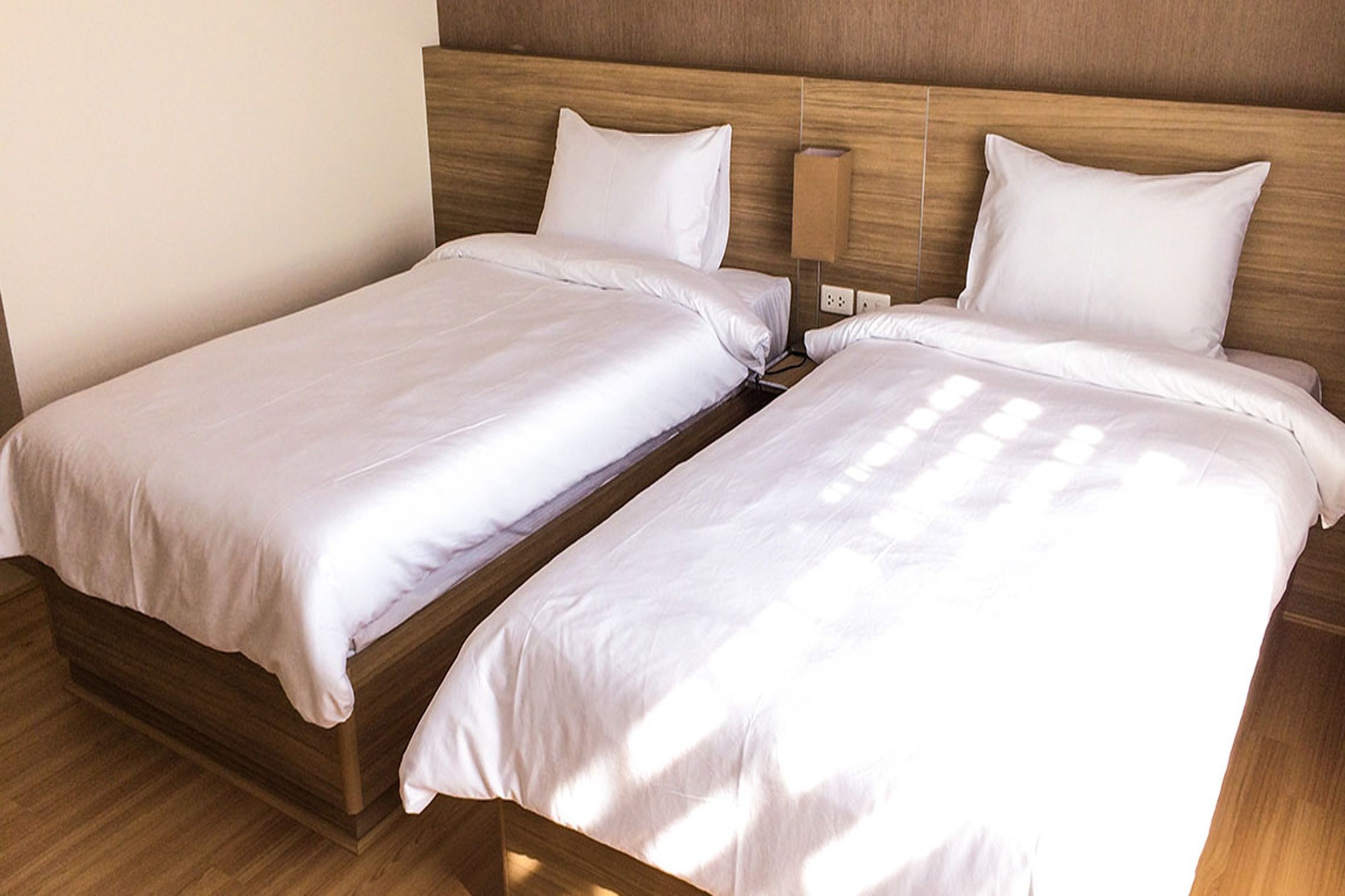 A double bed with white bedding in a room with wooden headboard and nightstand.