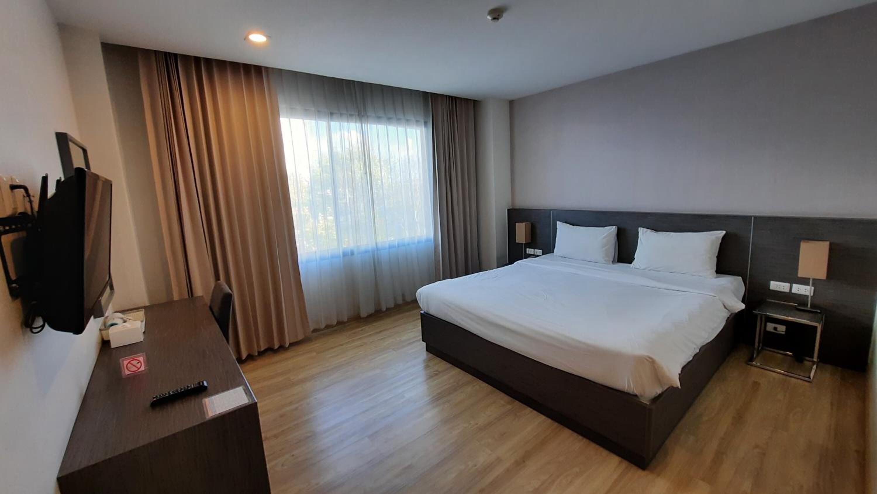 Une chambre d’hôtel avec un grand lit, un bureau avec une télévision et une fenêtre avec des rideaux.