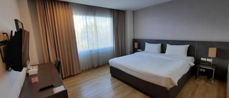 Une chambre d’hôtel avec un grand lit, un bureau avec une télévision et une fenêtre avec des rideaux.