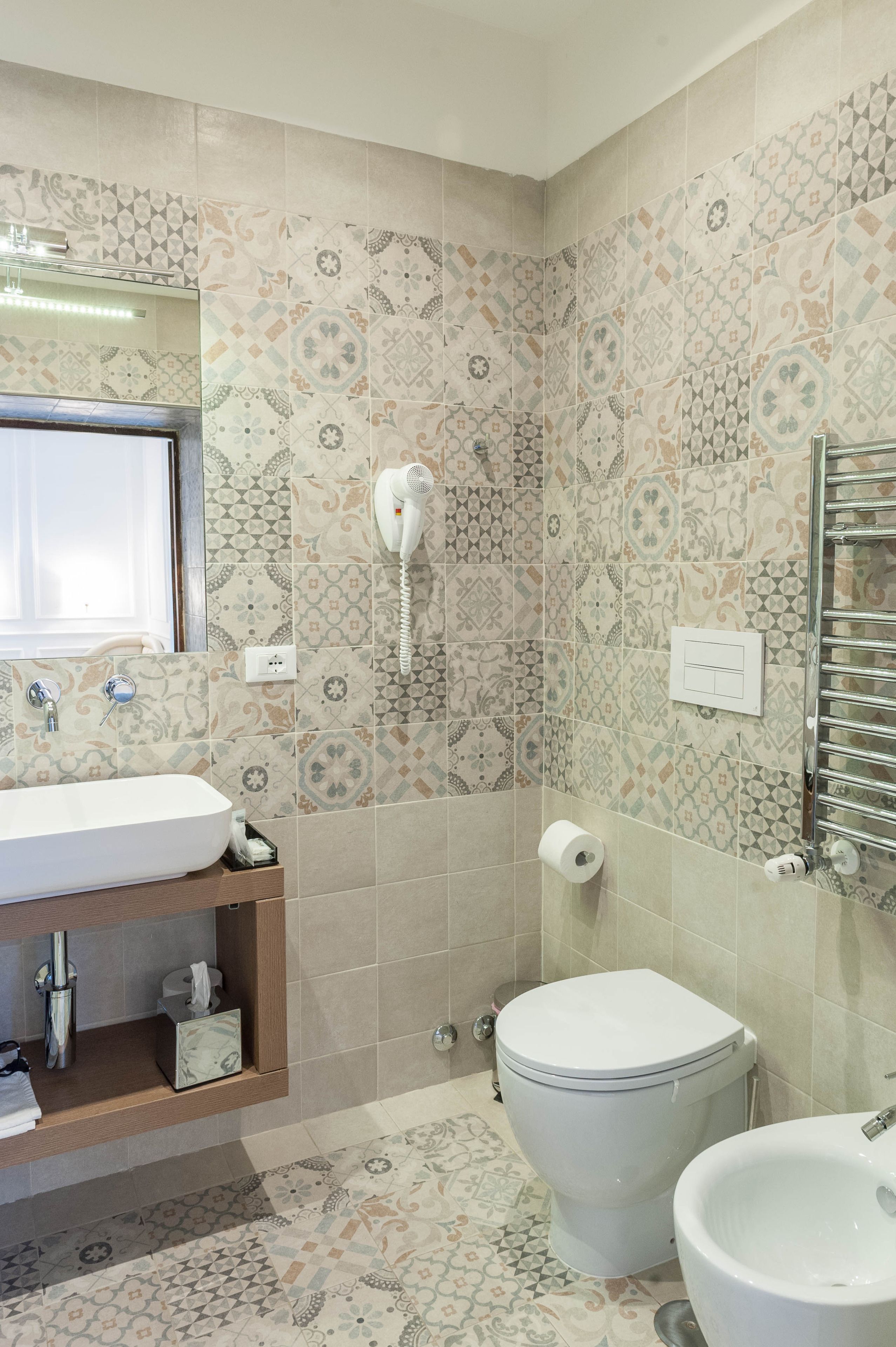 Une salle de bain avec des carreaux décorés, des toilettes, un bidet, un lavabo et un porte-serviettes.
