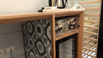 A kitchenette with a microwave, kettle, and coffee maker. There are clear storage containers and a refrigerator.