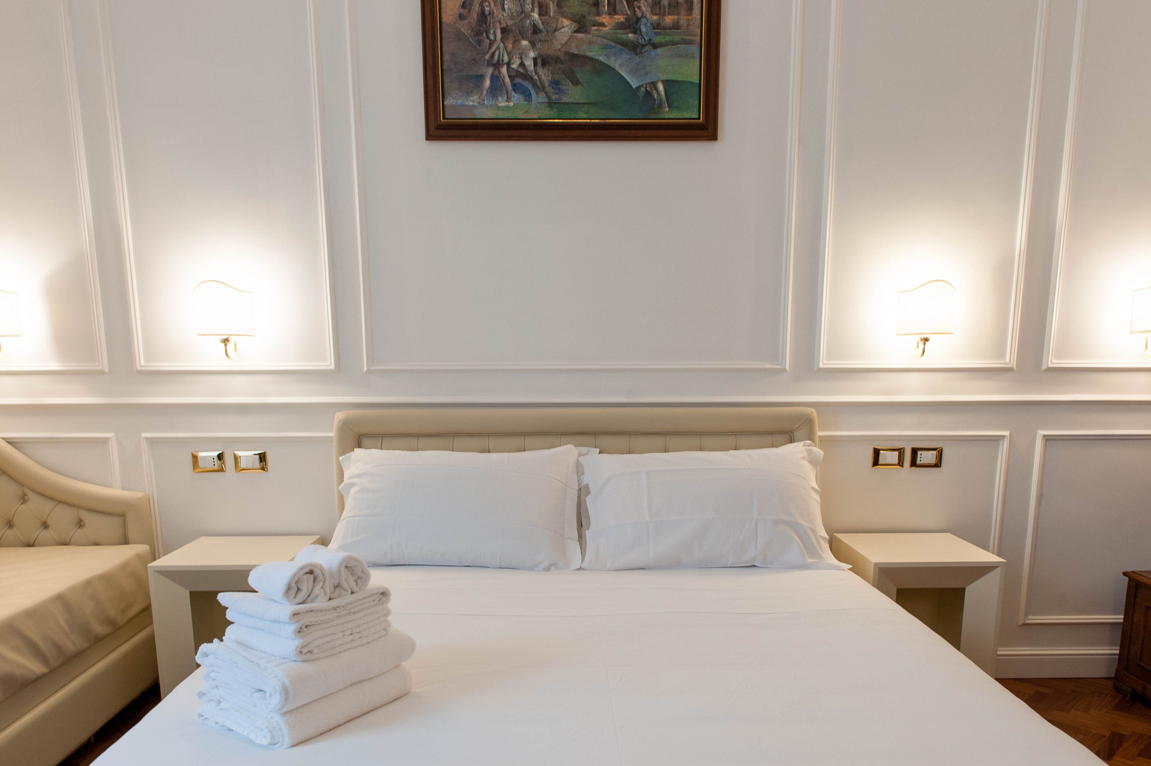 A hotel room with a large bed, two bedside tables, a chair, and a painting on the wall.