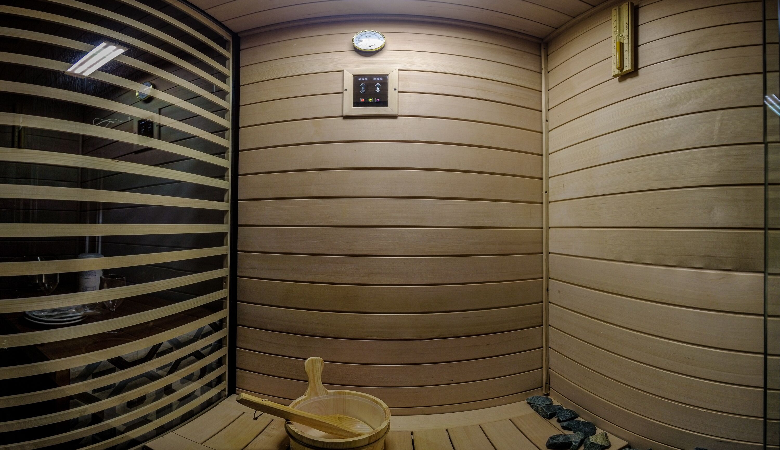 A sauna room with wooden walls, a control panel, and a wooden basin.