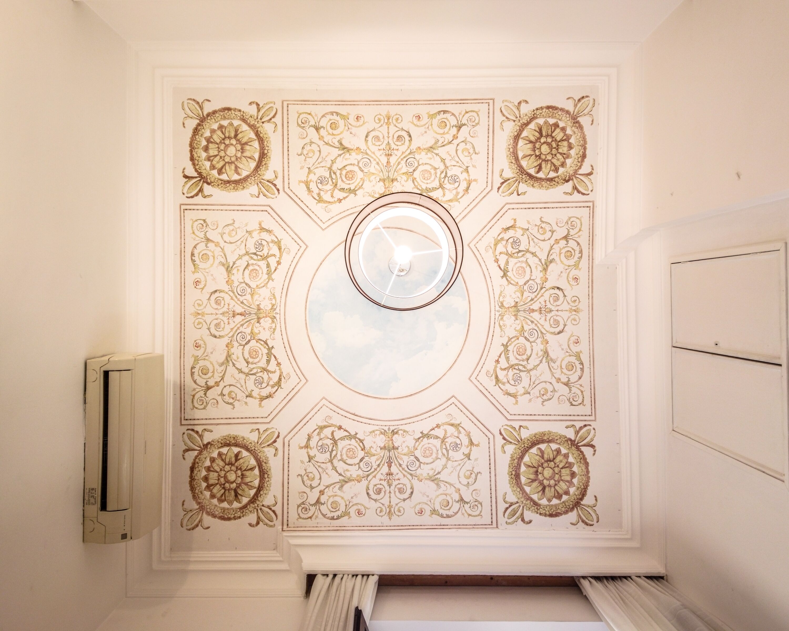 A room with a decorative ceiling featuring floral patterns and a central circular skylight.