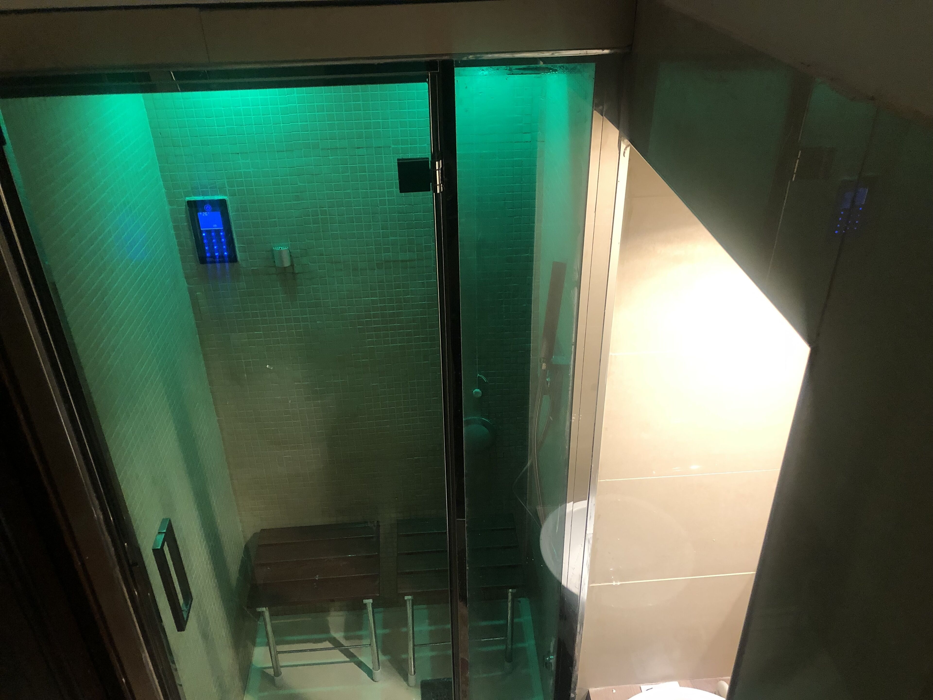 Un ascensore con pareti in vetro, illuminazione verde all'interno, un cestino della spazzatura e una panca.