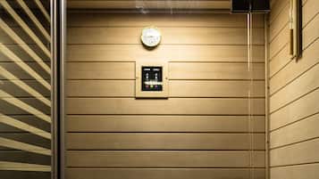 A sauna room with wooden walls, a ceiling light, a clock, and a control panel.
