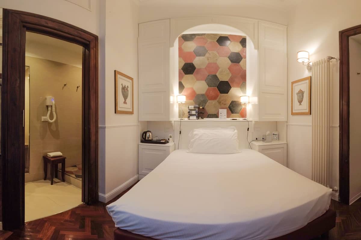 A hotel room with a large bed, a vanity with a mirror, a small table with a kettle, and a wall with a hexagonal tile pattern.