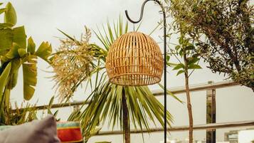 A wicker chair with a cushion, a hanging woven light fixture, and a patterned pillow.