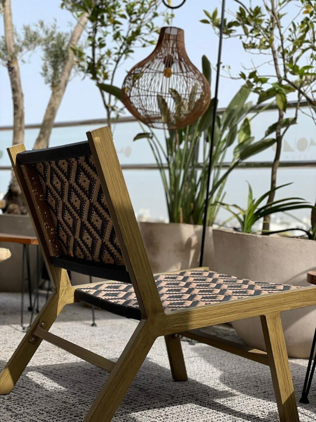 A wooden chair with a patterned backrest and seat, placed on a textured outdoor surface.