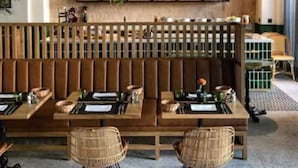 Un interior moderno con una zona de estar con banco de madera, iluminación colgante y una pared de estanterías con diversos objetos.