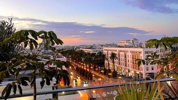 Un paisaje urbano al atardecer con vista a una calle bordeada de palmeras y edificios.