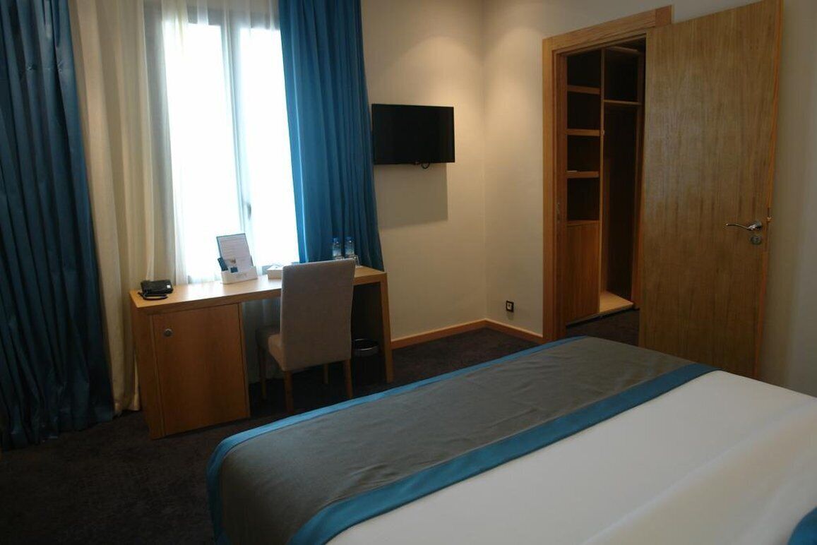 Una camera d'albergo con un letto, una scrivania con una sedia, una televisione a parete e un armadio.